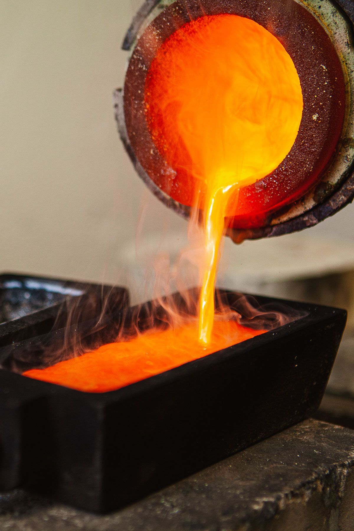 Weitere hochformatige Seitenansicht beim Gießen von flüssigem Gold aus dem Tiegel in eine längliche Barrenform